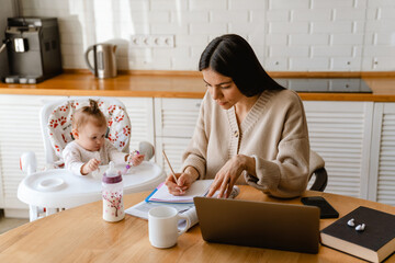Young mother working with laptop while keeping her baby at home