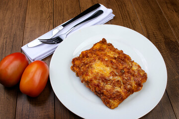 Lasagna in Bolognese sauce, made with ham cheese, tomato sauce and ground beef. Food served on white plate. Cutlery on napkin.