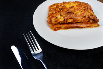 Tasty Lasagna in Bolognese sauce, made with ham cheese, tomato sauce and ground beef. Metal knife and fork.Traditional pasta cuisine.