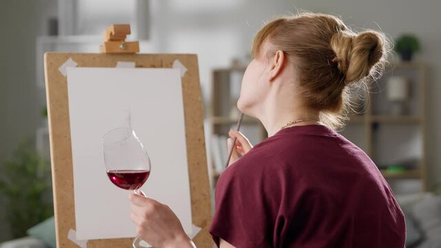 Portrait of a young woman with a glass of red wine. Artist at home in the living room.
