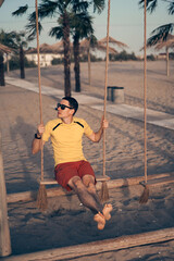 Young attractive man swinging on seesaw on the beach.