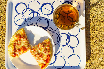 Tea mug and pizza slices on plate, outdoors