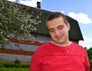 A young autistic guy smiles on a walk near the house in the summer, autistic behavior traits.