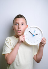 Shocked funny boy holding white clock alarm, copy space. Kid isolated over white background. Schedule and timing concept. 