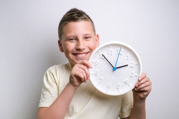 Smiling funny boy holding white clock alarm, copy space. Kid isolated over white background....