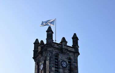 Old Stone Tower with Finials & Clock  with Pole & Flag against Blue Sky
