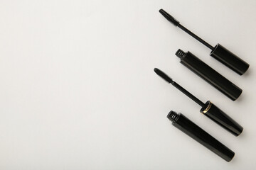 Black mascara wand and tube on grey background with copy space
