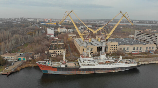 Ariel view of old cargo ship is moored at the dock on the river. There are two cranes nearby. Nikolaev city, Ukraine