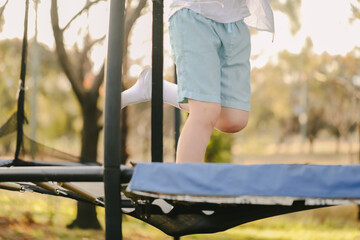 Little boy jumping high on trampoline in socks without face showing. Feet up in the air, childhood fun.