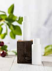Fototapeta na wymiar White tubes with cosmetics on a wooden podium against the background of foliage, cherry berries. Natural cosmetics. 