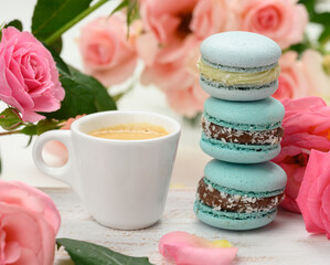 white ceramic cup with coffee and a stack of blue macarons on a white table