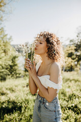 Naklejka na ściany i meble Young woman with curly hair, holding a bouquet of dandelions, outdoors.