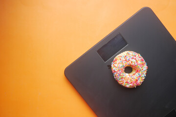  sweet donuts on weight scale on orange background  - obrazy, fototapety, plakaty