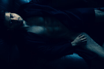 Portrait of attractive shirtless muscular man with beard and sixpack abs lying in leather armchair,...