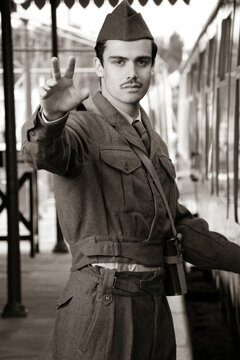 Handsome male British soldier in WW2 vintage uniform at train station next to train, waving goodbye