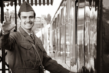 Handsome male British soldier in WW2 vintage uniform at train station next to train