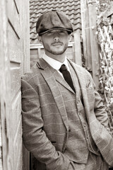 Handsome English gangster leaning on brick wall in back streets of birmingham