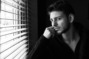 Portrait of handsome man with beard sitting next to window with blinds