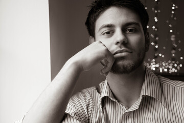 Portrait of handsome man with beard sitting next to window with lights in the background