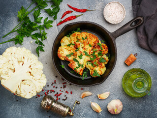 Cauliflower steak with parsley, garlic and spices. Olive oil, pink and black pepper, chili pepper and salt on a gray concrete background. Fried cabbage in a cast-iron skillet. Top view
