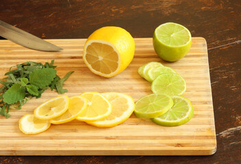 Ingredients for making gin and tonic on a wooden board chopped mint leaves, lime and lemon rings