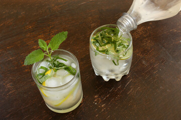 Close-up of a bottle of tonic pours into a glass with mint, lime and lemon. Homemade gin and tonic...