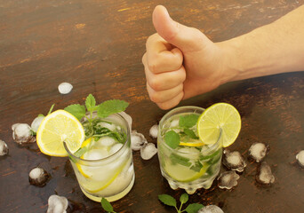 Two glasses with gin and tonic with mint, lime and lemon rings, ice cubes. near a man's hand with a...