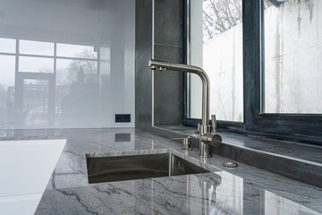 Modern kitchen concept with stainless steel kitchen sink and a water tap with marble countertop in...