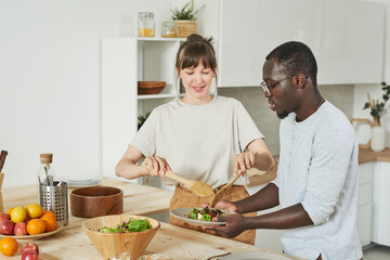 Fototapeta na wymiar Young couple preparing vegetable salad together in the kitchen