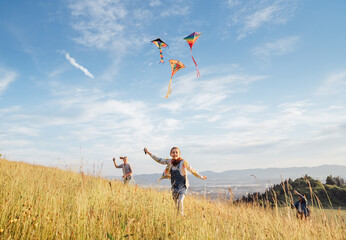 Smiling gils and brother boy with flying colorful kites - popular outdoor toy on the high grass...