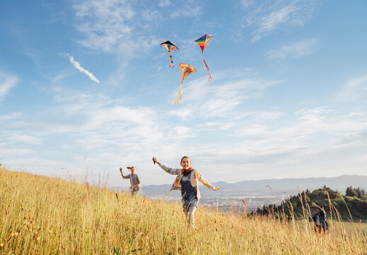 Smiling gils and brother boy with flying colorful kites - popular outdoor toy on the high grass meadow in the mountain fields. Happy childhood moments or outdoor time spending concept image.