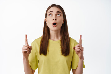 Portrait of amazed young woman pointing, looking up with excited face, checking out promo deal,...