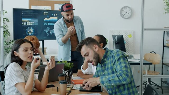 Serious businessman is making presentation talking while carefree colleagues are playing smart phone games and putting on make-up ignoring speaker.