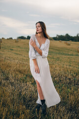 beautiful woman in a white dress walks across the field.