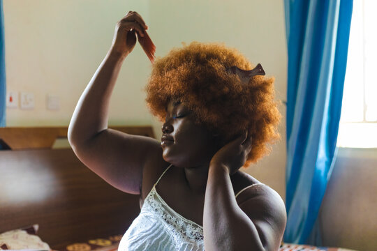 Ginger haired woman combing her hair with two afro combs.
