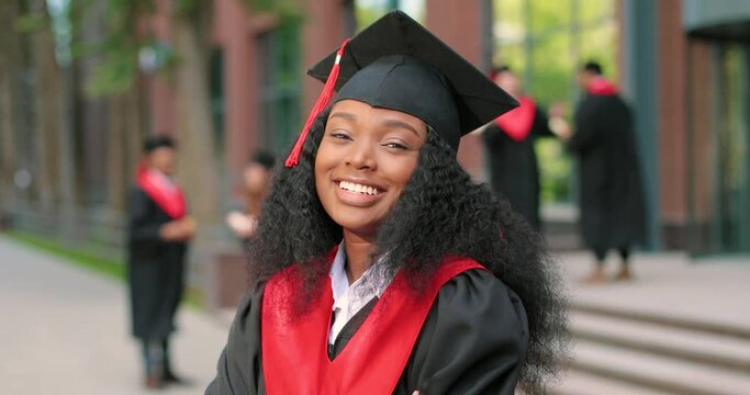 Young graduated curly girl holding her graduation degree convocation ceremony. Attractive multiracial student graduate posing towards the camera during the ceremony