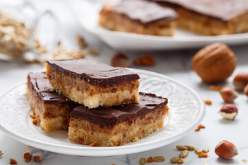 Homemade Vegan cocoa dates chocolate bars with coconut, hazelnuts, walnuts and sunflower seeds on a white background. Healthy dessert. The concept of plant food. Shallow depth of field