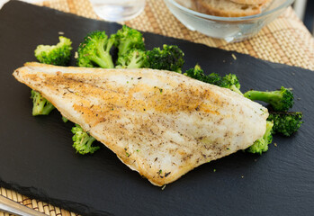 fried fillet of sea bass with garnish of broccoli on black warm stone plate