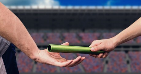 Mid section of hand passing a baton against sports stadium in background