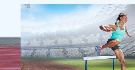 Caucasian female athlete jumping over a hurdle against sports stadium in background