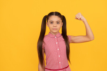 Serious girl child show power gesture flexing arm yellow background, strong