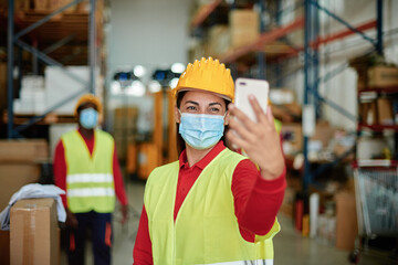Cheerful warehouse worker taking selfie with smartphone