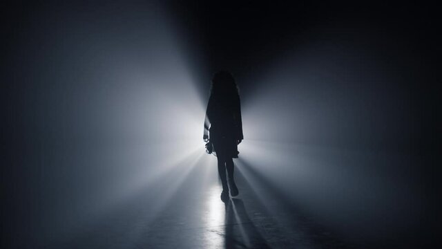 Silhouette girl walking darkness. Woman going straight on camera dark background