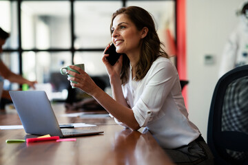 Happy businesswoman working on laptop. Portrait of beautiful businesswoman drinking coffee and...