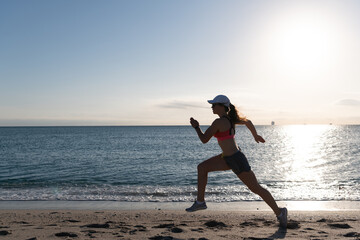 Energetic running woman in activewear run on beach sand along seaside, runner