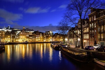 Fototapeta premium city ​​at night lights in buildings that reflect illumination on the European river containing trees and boats and on the street cars and people