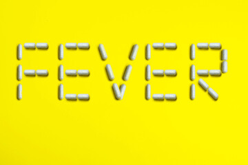 Pills capsules word text FEVER on yellow background. Medical medicine concept.