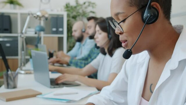 African American lady is concentrated on conversation working in call center with colleagues using laptop typing. Business and communication concept.