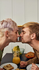 Same-sex caucasian male couple kissing at kitchen table