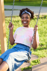 Portrait of African happy woman smiling at camera while riding on a swing in the park